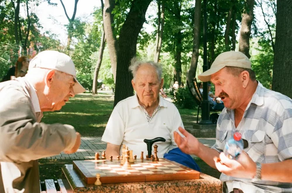 Trei vârstnici care joacă șah pe o masă din parc